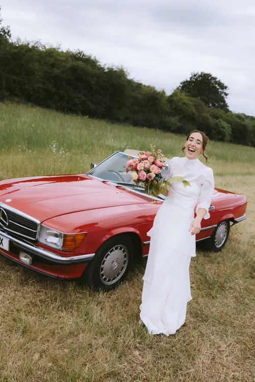 Bride beside a vintage red car on her wedding day