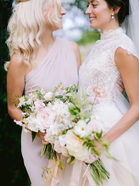 Bride with curled updo and pink bouquet alongside a guest
