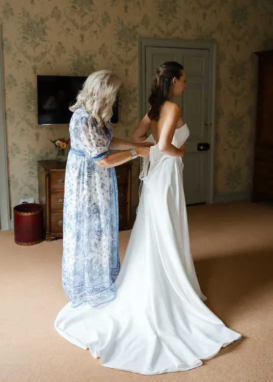 Stylist helping bride with dress and bridal hair before ceremony