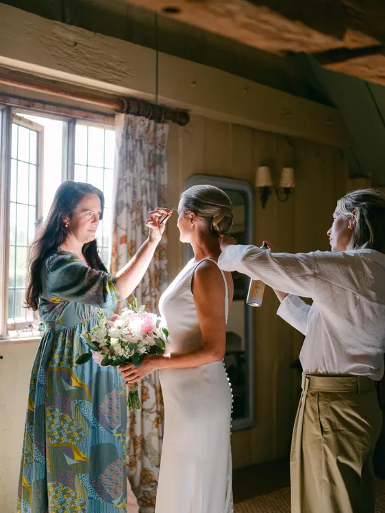 Charlotte and bridal team preparing a bride near the window